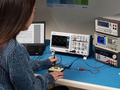 A woman operating a Tektronix data acquisition system with an oscilloscope and test equipment on a lab bench