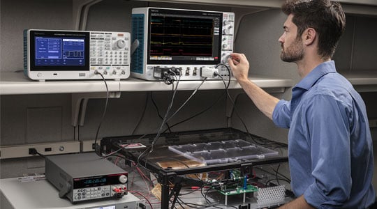 An engineer adjusting settings on an instrument cluster of Tektronix bench testing equipment.