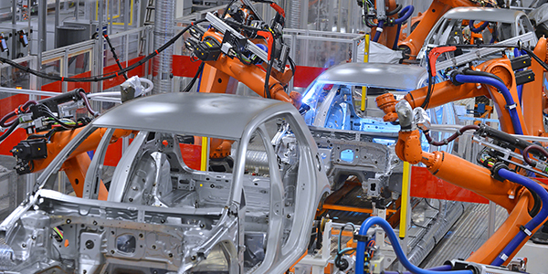 An industrial automotive assembly line with multiple orange robotic arms working on the metallic frame of a car